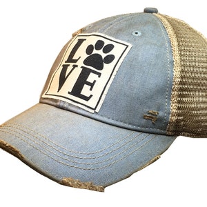 May include: A blue and brown distressed trucker hat with a white patch that says "LOVE" with a paw print in the "O".