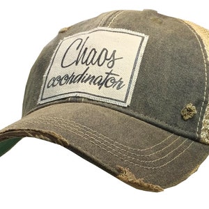 May include: A distressed brown and beige trucker hat with a white patch that reads "Chaos coordinator" in black script.