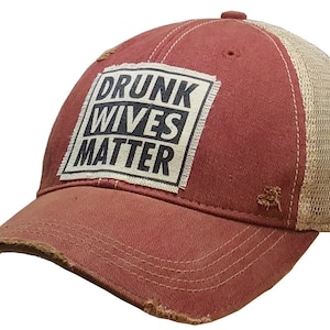 May include: A red and beige distressed trucker hat with a white patch that reads "DRUNK WIVES MATTER" in black text.