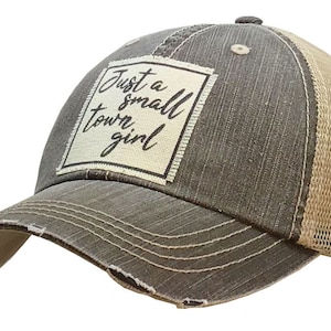 May include: A brown and beige trucker hat with a distressed look. The hat has a white patch on the front with the text "Just a small town girl" in black.