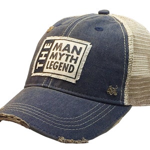 May include: A blue and beige distressed trucker hat with a white patch that reads "The Man Myth Legend".
