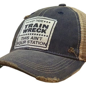 May include: A blue and brown distressed trucker hat with a white patch that reads "Hey There... Train Wreck... This Ain't Your Station".