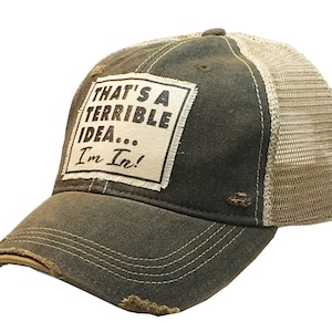 May include: A dark green and beige trucker hat with a distressed look. The hat has a white patch with the text "That's a terrible idea... I'm in!"