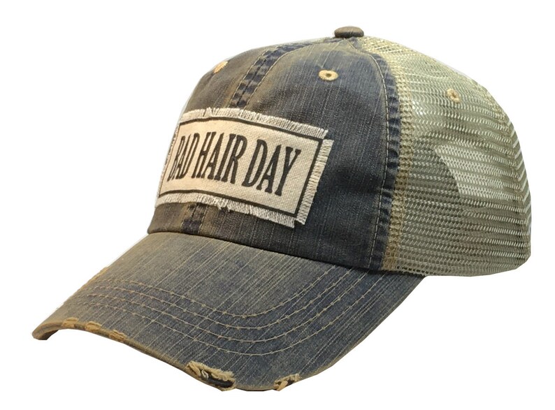 Op de afbeelding: Een blauwe denim en mesh trucker cap met een verweerde look. De pet heeft een witte patch met de tekst "Bad Hair Day" in zwart.