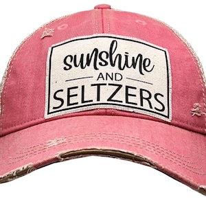 May include: A distressed pink baseball cap with a mesh back. The front features a white rectangular patch with the words "sunshine" and "seltzers" in black script and block letters. The cap has a curved brim and a distressed look.