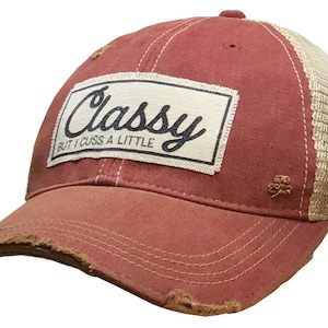 May include: A red and beige distressed trucker hat with a white patch that says "Classy But I Cuss A Little" in black lettering.