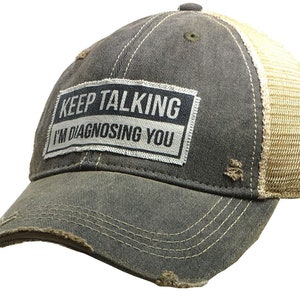May include: A black and tan distressed trucker hat with a white patch that reads "KEEP TALKING I'M DIAGNOSING YOU".