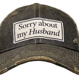 May include: Distressed olive green trucker hat with a white patch that reads "Sorry about my Husband" in black text. The hat has a mesh back and a curved brim with distressed edges.