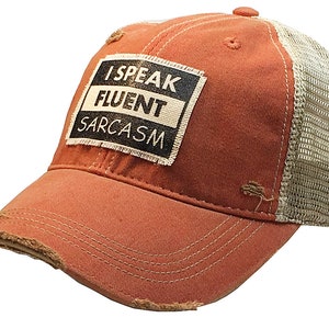 May include: A red and beige trucker hat with a distressed look. The hat has a patch on the front that says "I Speak Fluent Sarcasm".