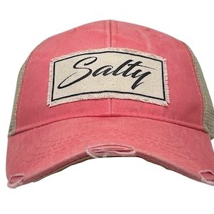 May include: A distressed coral-colored baseball cap with a beige mesh back. The front features a rectangular patch with the word "Salty" in black script. The cap has a pre-curved bill and distressed details.