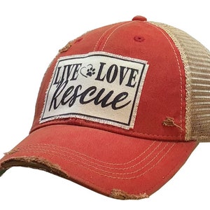 May include: Red and beige distressed trucker hat with a white patch that says "Live Love Rescue" in black lettering.