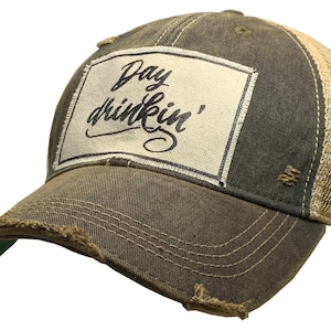 May include: A brown and beige distressed trucker hat with a white patch that says "Day drinkin'" in black cursive lettering.