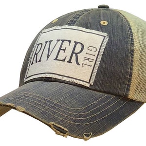 May include: A blue and beige distressed trucker hat with a white patch that says "River Girl" in black lettering.
