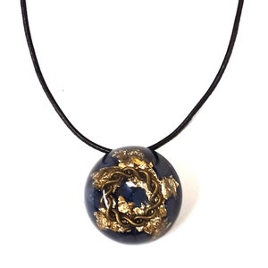 May include: A black leather cord necklace with a round pendant. The pendant is made of clear resin with a gold-colored design inside. The design is a Celtic knot.