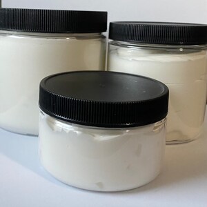 May include: Three clear plastic jars with black lids filled with white cream. The jars are different sizes.