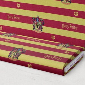 May include: Red and gold striped fabric with the Harry Potter logo and the Gryffindor crest repeated throughout. The fabric is rolled up and labeled "FSSSC 36 Gryffindor Stripe".