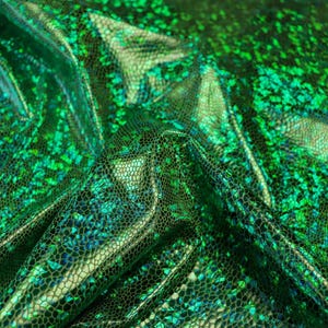 Könnte beinhalten: Ein leuchtend smaragdgrüner Stoff mit einem reflektierenden, holografischen schuppenartigen Muster. Das Material hat einen metallischen Glanz mit einer strukturierten Oberfläche, die das Licht einfängt und ein mehrdimensionales Erscheinungsbild auf dem gefalteten Textil erzeugt.