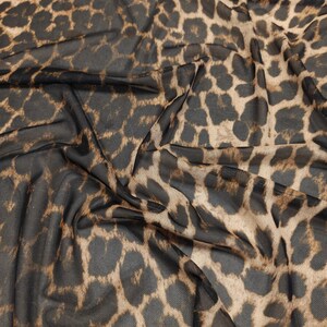 May include: Close-up of a sheer fabric with a leopard print pattern. The fabric is a dark brown mesh with tan and dark brown spots. The fabric is draped, showing the texture and pattern.