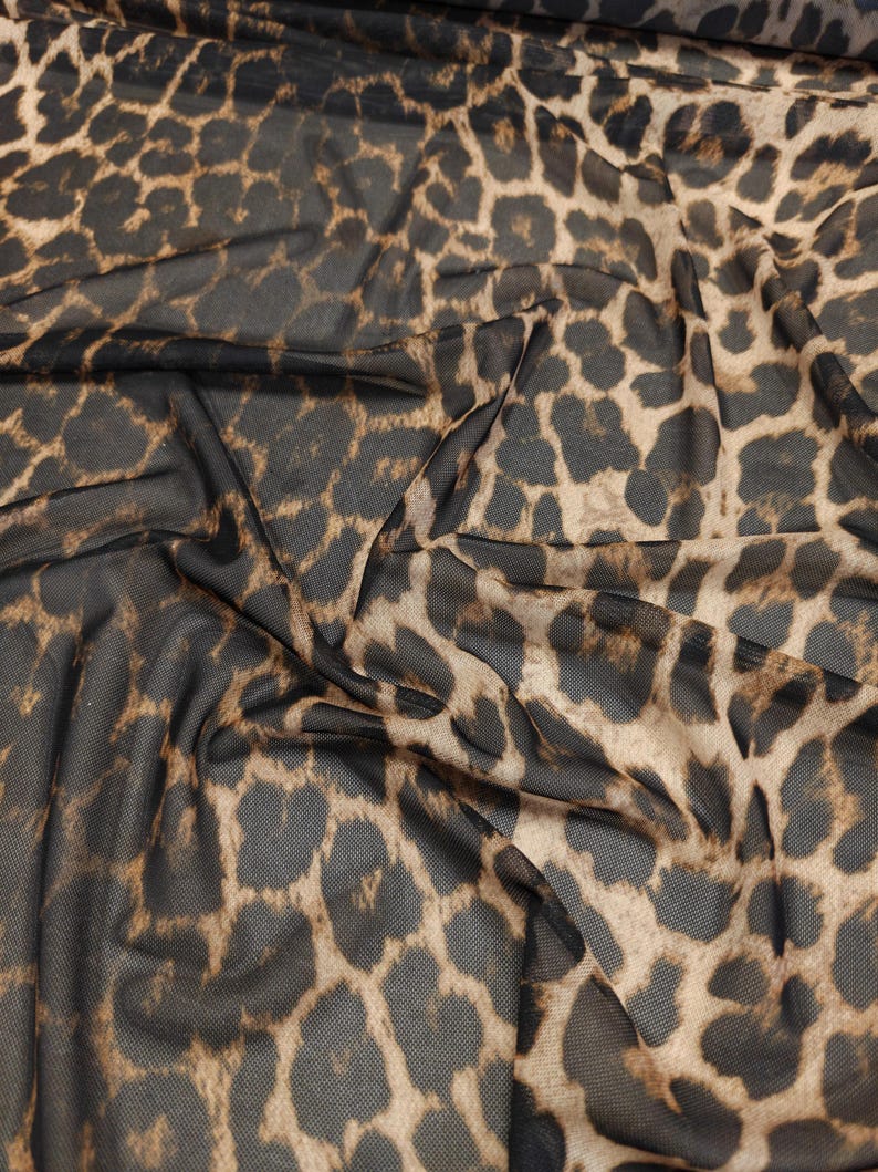 May include: Close-up of a sheer fabric with a leopard print pattern. The fabric is a dark brown mesh with tan and dark brown spots. The fabric is draped, showing the texture and pattern.