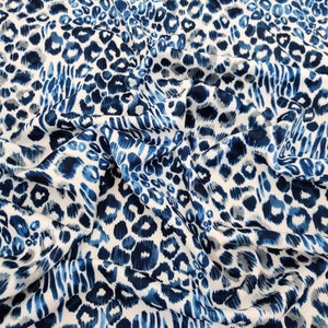 May include: A fabric with a blue and white leopard print design. The pattern features various shades of blue spots and brushstrokes against a white background. The fabric is gathered, creating soft folds and shadows.