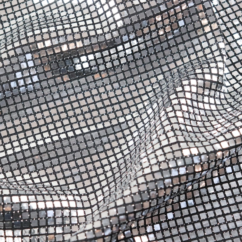 May include: Silver fabric with a grid pattern of small, shiny squares. The fabric is wrinkled and has a metallic sheen.