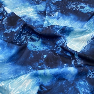 Peut inclure: Gros plan sur un tissu avec un motif aquatique. Le tissu présente des nuances de bleu, du clair au foncé, créant un design fluide et aquatique. Le tissu est probablement de la soie ou une matière similaire, avec un drapé doux et fluide.