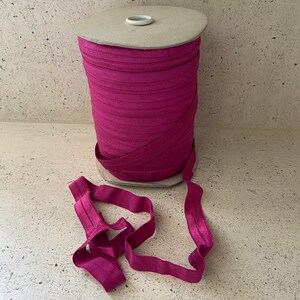 May include: A spool of pink elastic fabric, wound around a cardboard tube. The elastic is folded and laid out in a loose loop.