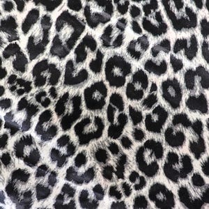 May include: A fabric featuring a repeating leopard print pattern in shades of black, white, and light grey. The design consists of irregular, dark, rounded spots outlined in black against a lighter, textured background, creating a classic animal print.