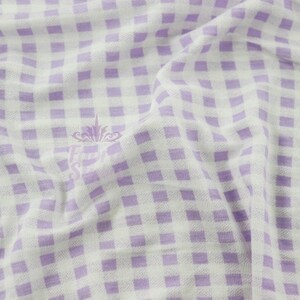 Könnte beinhalten: Nahaufnahme eines weiß-lila Vichy-Stoffs. Der Stoff hat ein Karomuster und ist leicht zerknittert. Ein Logo ist in der Mitte des Stoffes sichtbar.