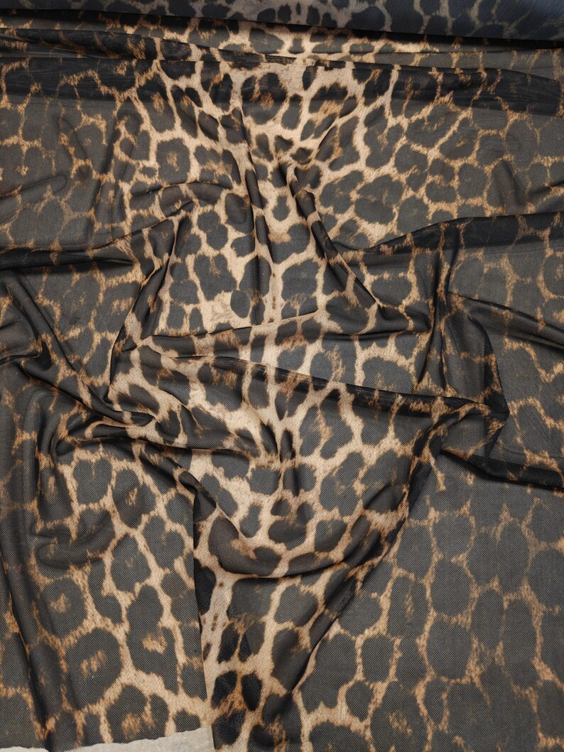 May include: A sheer fabric with a leopard print pattern. The fabric features a dark brown background with tan and brown spots. The material is draped, showing the texture and pattern of the fabric. This textile is suitable for apparel and craft projects.