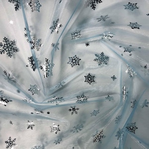 May include: A light blue sheer fabric featuring a repeating pattern of metallic silver snowflakes. The material is gathered and draped, creating soft folds and shadows that highlight the reflective quality of the silver snowflake print.