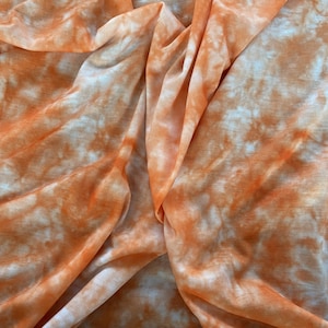 Puede incluir: Un primer plano de una tela de color naranja y blanco teñida anudada. La tela está doblada y drapeada, mostrando el patrón de remolino del tinte.