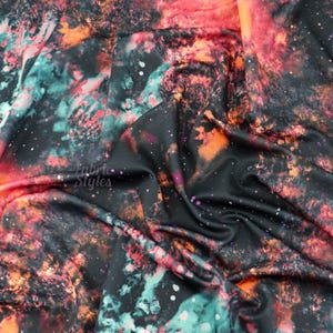 Op de afbeelding: Zwarte stof met een galaxy print in oranje, rood en turquoise kleuren. De stof is gekreukt en heeft een glanzende afwerking.