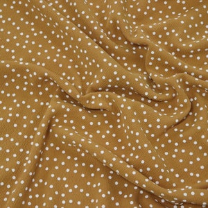 Peut inclure: Un gros plan sur un tissu brun avec un motif de pois blancs. Le tissu est froiss&eacute; et a une texture douce.