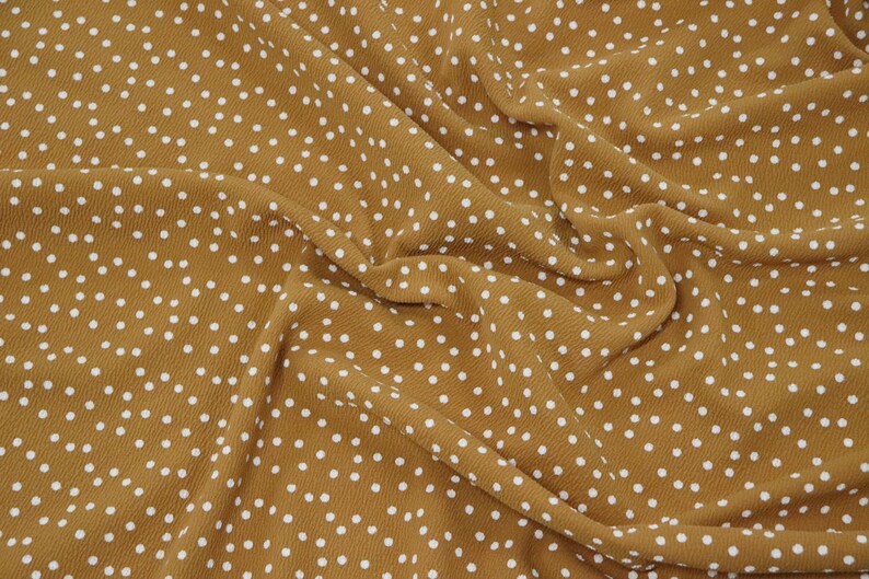 Peut inclure: Un gros plan sur un tissu brun avec un motif de pois blancs. Le tissu est froiss&eacute; et a une texture douce.