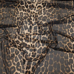 May include: Close-up of a sheer fabric with a leopard print pattern. The fabric features a dark brown and tan spotted design on a black background. The material is draped, showing the texture and flow of the fabric.