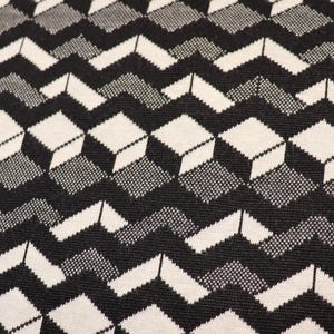 Könnte beinhalten: Ein Textilstoff mit einem sich wiederholenden geometrischen Muster aus schwarzen, weißen und grauen Würfeln, die in einer Zickzack-Formation angeordnet sind. Das Design erzeugt einen dreidimensionalen optischen Täuschungseffekt.