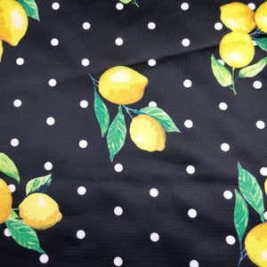 May include: A black fabric featuring a repeating pattern of bright yellow lemons with green leaves and small white polka dots. The lemons are depicted in clusters, showcasing their oval shape and textured rinds against the dark background.