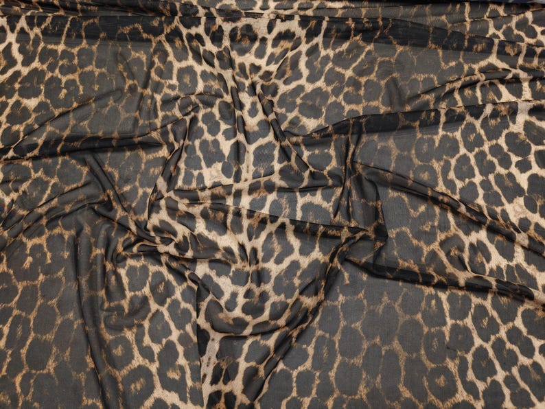 May include: Close-up of a sheer fabric with a leopard print pattern. The fabric features a dark brown and tan spotted design on a black background. The material is draped, showing the texture and flow of the fabric.