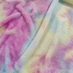 Puede incluir: Primer plano de una manta suave y esponjosa con un diseño tie-dye. Los colores incluyen rosa, morado, amarillo y azul. La manta tiene una textura de felpa y parece estar hecha de un material difuso.