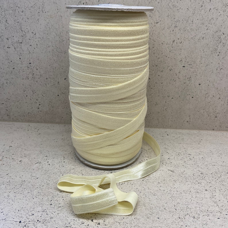 May include: A roll of pale yellow elastic, also known as fold over elastic, is wound around a cardboard core. The elastic is a soft, stretchy fabric with a subtle sheen.