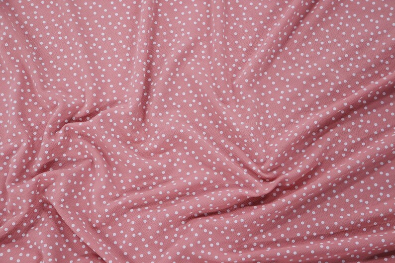 Peut inclure: Tissu rose avec un motif de pois blancs. Le tissu est froiss&eacute; et a une texture douce.