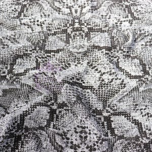 May include: A fabric featuring a repeating black and grey snakeskin pattern. The material has a textured appearance with visible folds and creases, creating a dynamic surface that mimics the natural scales of a snake in a monochromatic color palette.