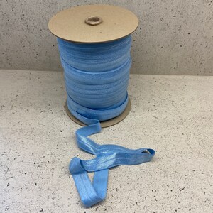 May include: A spool of light blue elastic with a shimmery finish. The elastic is wound around a cardboard spool.