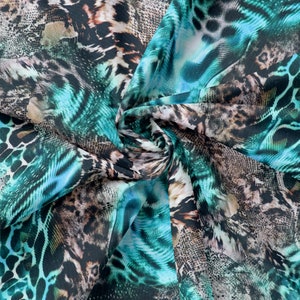 Pode incluir: Um tecido vibrante com um design de estampa animal mista. O padrão combina manchas de leopardo, escamas de cobra e listras de tigre em tons de verde-azulado, marrom e preto. O tecido é drapeado, criando dobras e sombras suaves.