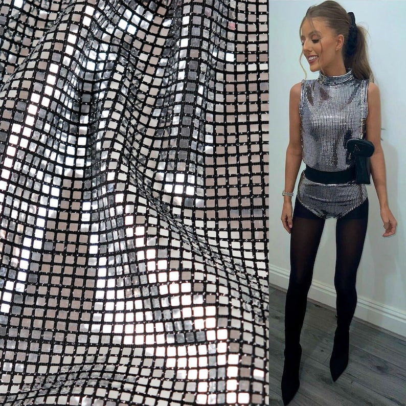 May include: Silver sequined fabric with a square pattern. The fabric is draped over a surface and has a slight sheen.