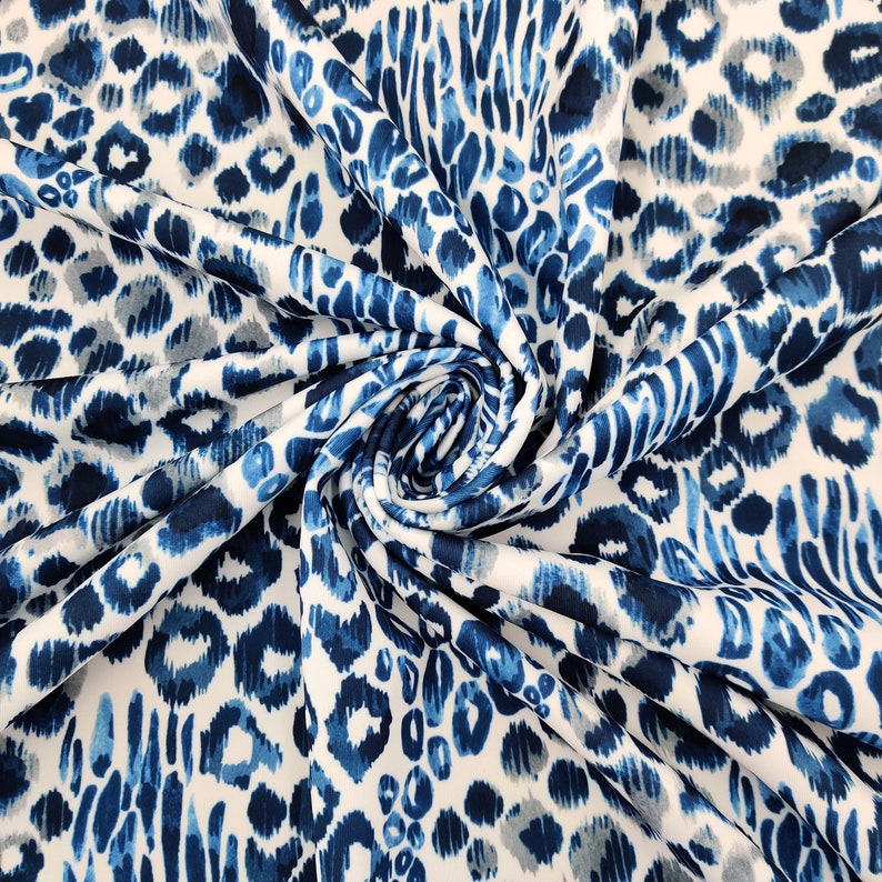 May include: White fabric with a blue animal print design. The fabric features a repeating pattern of blue spots and elongated shapes, with some gray accents. The fabric is folded and swirled, creating a textured appearance.