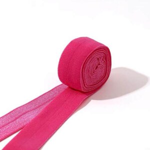May include: A roll of pink elastic trim with a shiny finish. The trim is folded in half and the ends are overlapping.