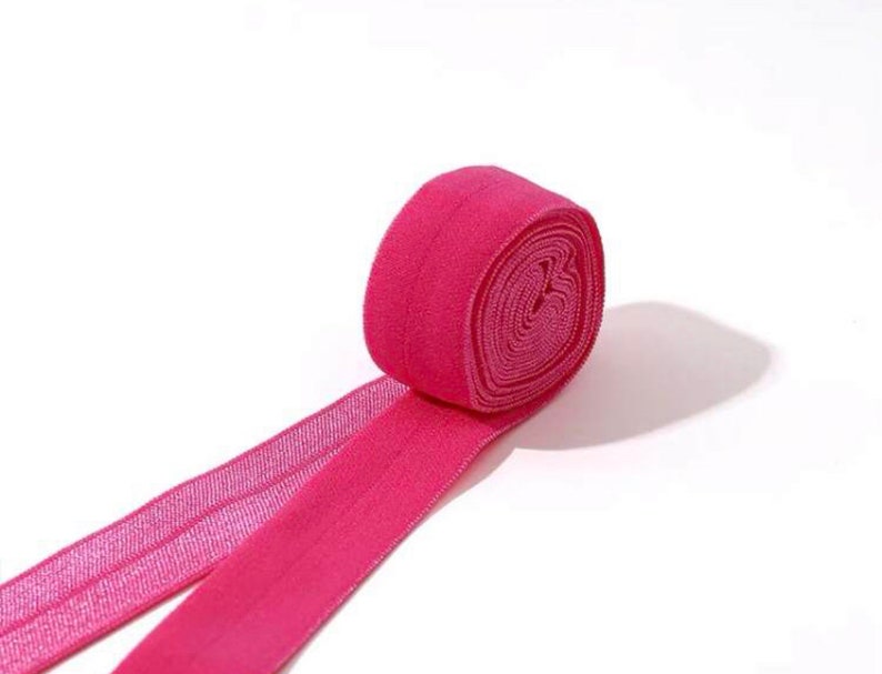 May include: A roll of pink elastic trim with a shiny finish. The trim is folded in half and the ends are overlapping.