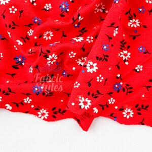 May include: Red fabric with a floral pattern. The fabric features white and blue flowers with black stems and leaves. The text "Fabric Styles" is visible on the fabric.
